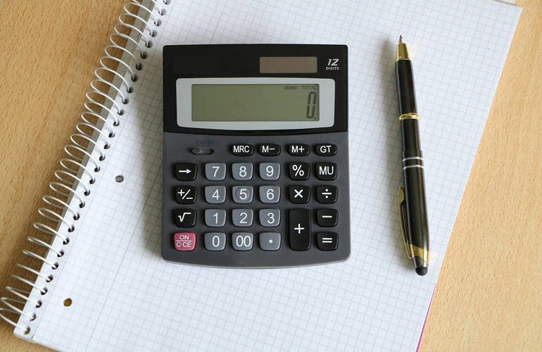 Une calculatrice et un stylo sont posés sur un cahier.