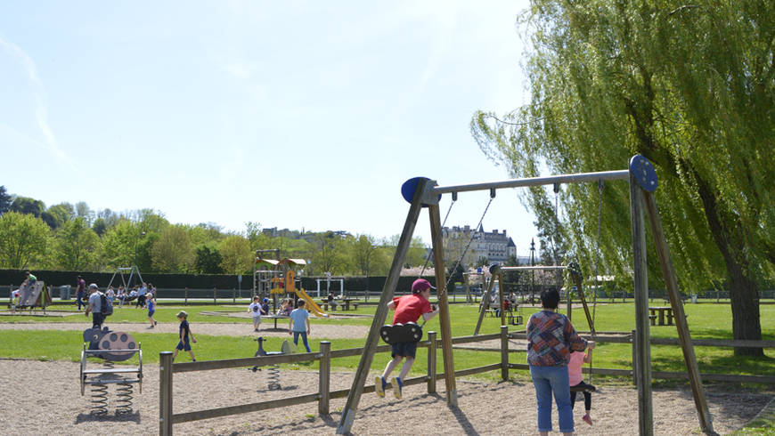 Aire de jeux sur l'Île d'Or avec vue sur le château. De nombreux enfants jouent sous un ciel bleu.