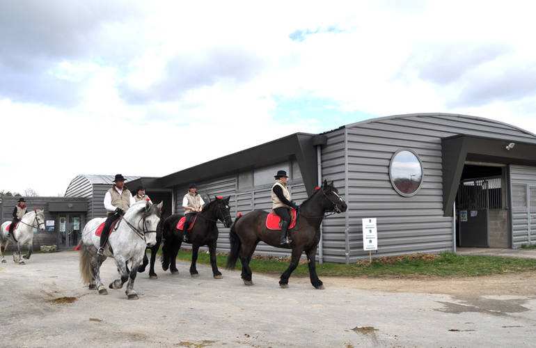 Devant le bâtiment des Haras, plusieurs chevaux montés par des cavaliers.