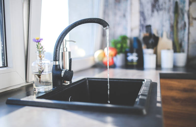 Dans une cuisine, vue sur un évier avec un robinet d'où coule de l'eau.