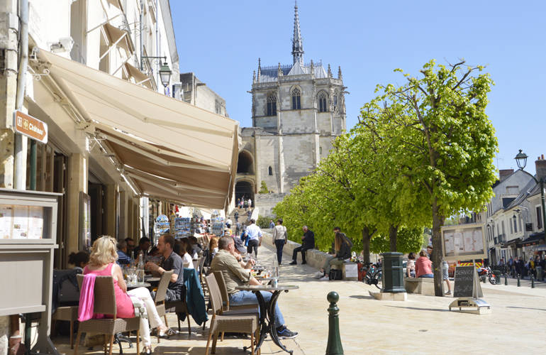 Vue sur la place du Château Royal d'Amboise avec au premier plan des touristes à la terrasse d'un café.