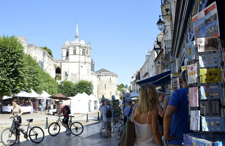 Des touristes se promènent à pied et en vélo sur la place Michel Debré. C'est l'été, le ciel est bleu.