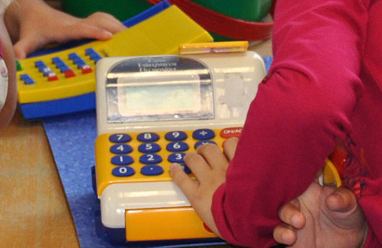 Gros plan sur les mains d'un enfants avec une caisse enregistreuse en jouet.