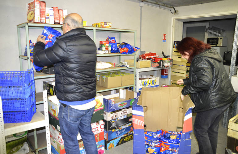 Deux personnes sont dans la réserve alimentaire du Centre Communal d'Action Social. Ils rangent des denrées alimentaires sur des étagères.