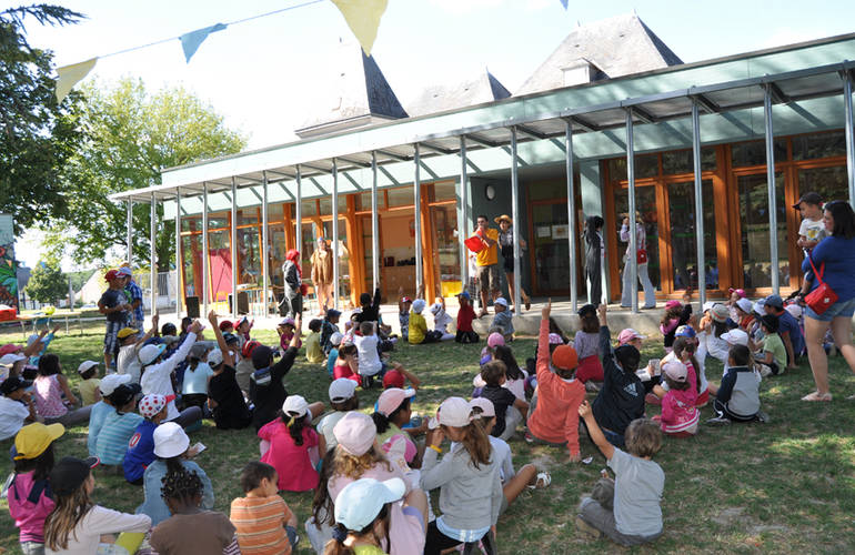 Beaucoup d'enfants sont assis devant le bâtiment de l'accueil de loisirs. Il fait beau. Un animateur leur parle.