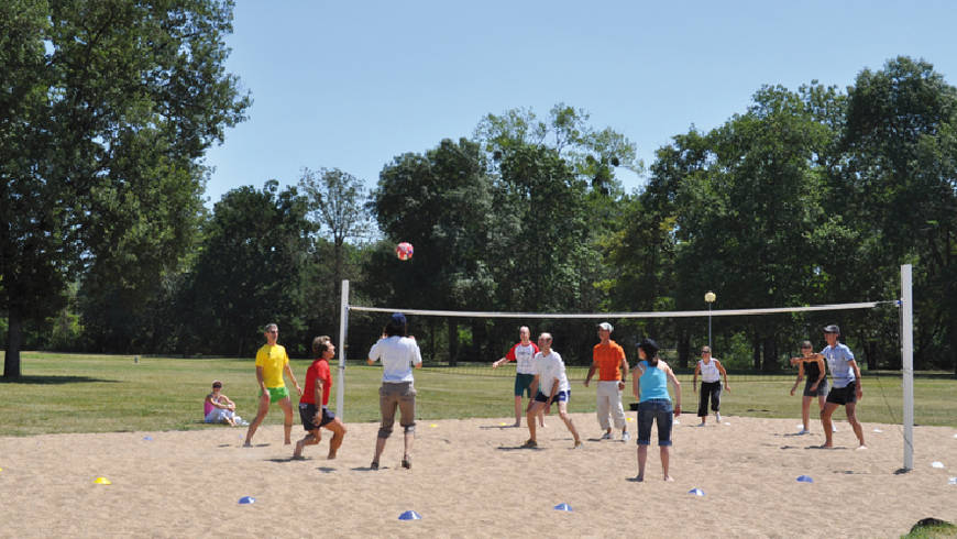 Un groupe de personnes joue au volley sur un espace ensablé.