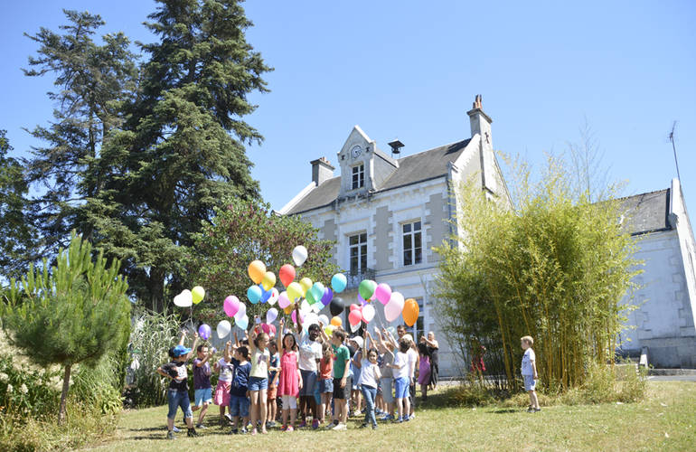 Des enfants sont regroupés devant l'école Ambroise Paré. Le ciel est bleu. Ils tiennent dans leur main des ballons multicolores.