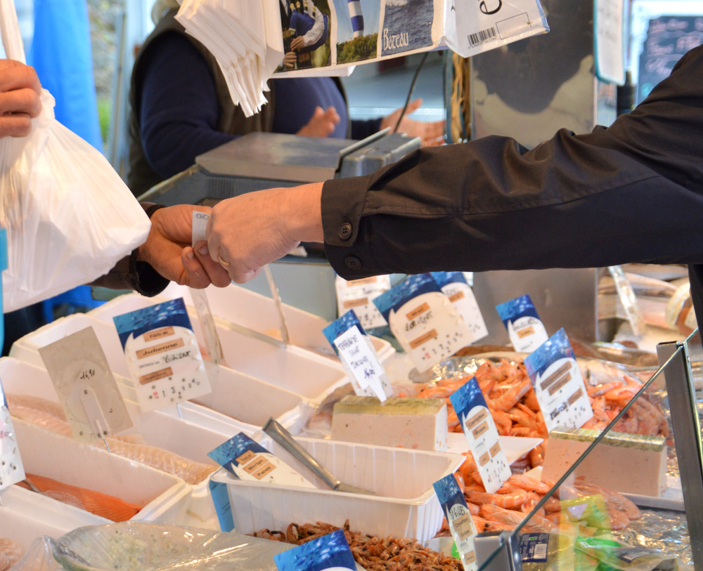 Vue sur un étalage d'une poissonnerie du marché. Un main tient un sac et l'autre l'argent de l'achat.